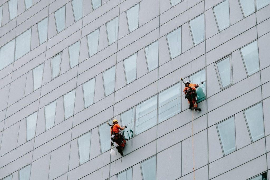 A rope access technician suspended by ropes inspects the exterior facade of a residential high rise building in Melbourn