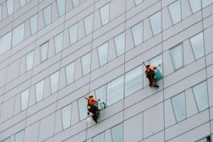 A rope access technician suspended by ropes inspects the exterior facade of a residential high rise building in Melbourn