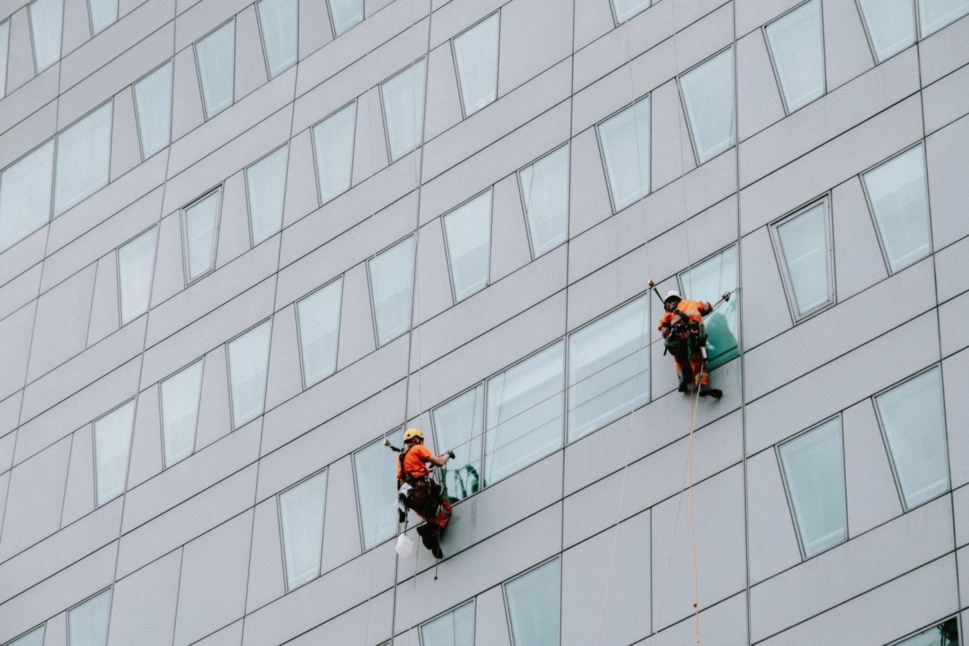 A rope access technician suspended by ropes inspects the exterior facade of a residential high rise building in Melbourn
