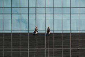 A rope access technician in safety gear cleans the exterior windows of a modern residential high-rise building in Melbou